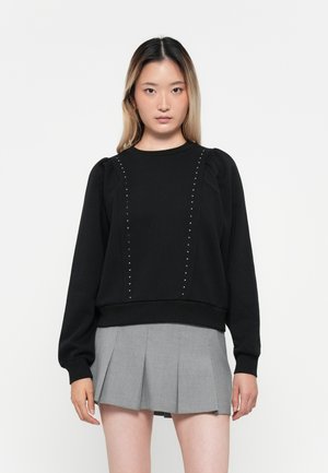 Sweat-shirt noir avec un col ras du cou côtelé, des manches bouffantes et des détails cloutés sur le devant. Associé à une jupe plissée grise.