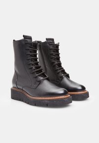 Botas negras de cuero con cordones y un acabado texturizado, que presentan una puntera redondeada y una suela de plataforma gruesa con costuras en contraste.
