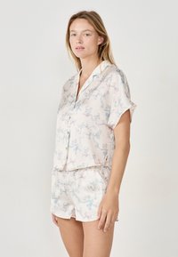 Ensemble de pyjama en tissu doux et léger, présentant une palette de couleurs pastel avec des illustrations amusantes de chats et de rubans. Haut à manches courtes et shorts.