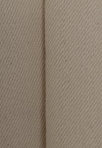 Beige strukturierter Stoff mit einem diagonalen Webmuster, das zwei gefaltete Abschnitte zeigt, die seine Weichheit und feinen Variationen betonen.