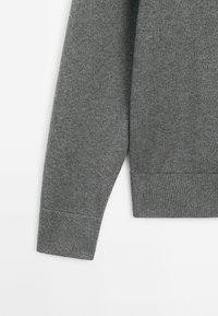 Manche de pull gris à manches longues avec poignets et ourlet côtelés, fabriquée en tissu tricoté doux.