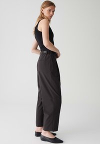 Un débardeur noir associé à un pantalon taille haute marron foncé avec une finition élégante, des poches latérales et des ballerines noires simples.