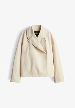 Veste courte beige avec larges revers, manches longues et poches verticales à coutures sur le devant, présentée sur fond blanc uni.