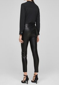 Zwarte blouse met lange mouwen en plooien aan de achterkant, gecombineerd met hoge, aansluitende zwarte leren broek en zwarte hakken met enkelbandjes.