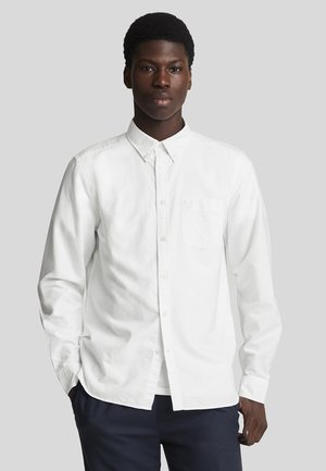 Camisa blanca de botones con mangas largas, collar y un bolsillo en la parte frontal. Fabricada con tejido suave, presenta un corte relajado y un diseño minimalista.