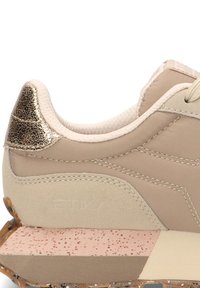 Zapatilla beige con un acento dorado texturizado en el talón, presenta un material suave y una entresuela rosa de contraste con un diseño salpicado.