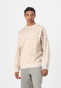 Beiger Pullover mit strukturiertem, hellbraunem Tiermotiv. Mit Rundhalsausschnitt, gerippten Bündchen und Saum. Kleines weißes Logo auf der Brust.