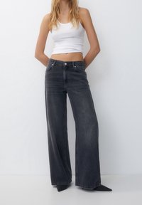 High-waisted, wide-leg black denim jeans with a faded finish, featuring a button closure and five pockets. Smooth texture and straight cut.