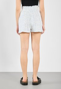 White shorts with a floral pattern in blue, featuring a smocked waistband and a relaxed fit, paired with black platform sandals.