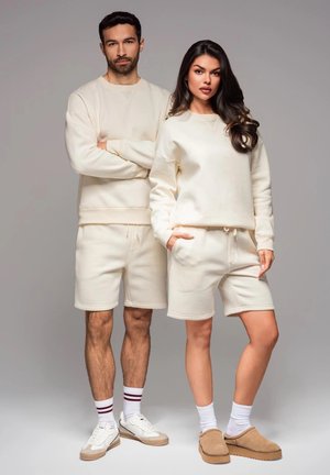 Des sweat-shirts et des shorts de couleur crème fabriqués à partir d'un tissu doux. L'homme porte un sweat-shirt à manches longues, tandis que la femme a un col rond et des poches.