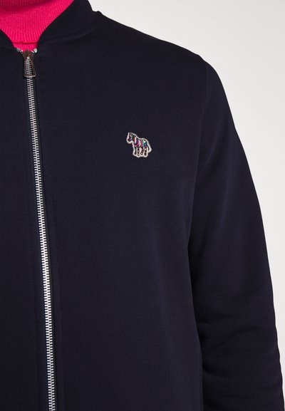 Jūras spēku zip-up džemperis ar ribotu tekstūru. Uz kreisās krūts puses ir neliels, krāsains izšuvuma zirga logotips.