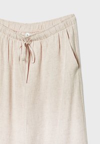 Lys beige linnedbukser med elastisk talje, snorelukning og sidelommer på en hvid baggrund.