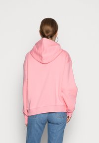 Sudadera rosa de gran tamaño con una capucha grande, textura suave, dobladillo acanalado y hombros caídos, combinada con jeans azules.