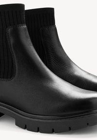 Bottes noires en cuir à la cheville avec des panneaux latéraux élastiques, tissu côtelé, semelle en caoutchouc épaisse et bout rond. Texture lisse avec un léger éclat.