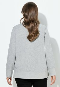 Sudadera gris con mangas largas, cuello redondo, puños acanalados y un dobladillo trasero ligeramente más largo. Tejido suave y texturizado.