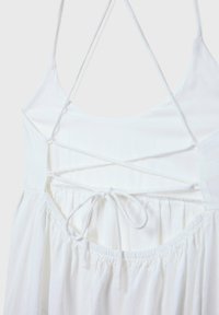 Robe blanche avec un corsage ajusté à bretelles spaghetti, un dos en croisillon et une jupe fluide et froncée avec une ceinture à nouer.