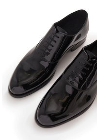 Scarpe da uomo in vernice nera con punta arrotondata, caratterizzate da un design con lacci e dettagli di cucitura discreti. Finitura liscia e lucida.
