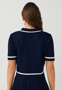 Marineblaues Polohemd mit kurzen Ärmeln und weißen Akzenten an Kragen und Ärmeln. Enganliegendes Design und gerippte Textur, von hinten gezeigt.