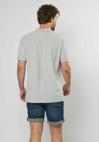 Rövid ujjú, világosszürke poloing textúrált felülettel, felhajtott farmer sorttal párosítva. Minimalista dizájn, látható logók vagy minták nélkül.