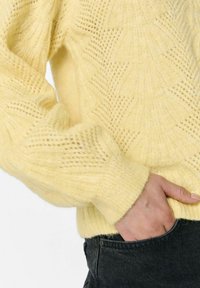Yellow knitted sweater with textured pattern and ribbed cuffs, displayed against a light background, showcasing softness and warmth.