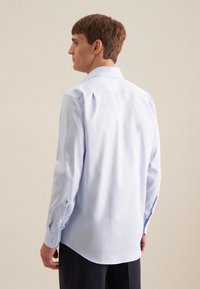 Camicia da uomo azzurro chiaro a maniche lunghe in tessuto morbido. Presenta un colletto classico, polsini con bottoni e un orlo curvo. Ricamo sottile sul polsino.