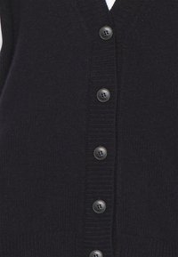 Cardigan bleu marine foncé avec un col en V, texture côtelée et six boutons ronds noirs sur le devant. Le tissu semble doux et tricoté.