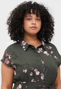 Green floral blouse with short sleeves, featuring pink and brown floral patterns, a collar, and a tied knot detail at the waist.