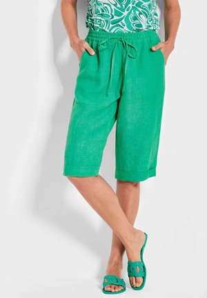 Shorts capri en lin vert avec une taille élastique et un cordon de serrage. Comprend des poches latérales et un ourlet retroussé. Associés à des sandales à enfiler assorties.