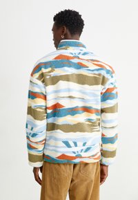 Pullover in pile con motivi multicolori di arancione, blu e verde, con colletto alto e superficie morbida e strutturata.