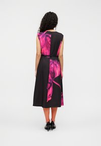 Robe noire sans manches avec un imprimé floral rose vif, taille cintrée par une ceinture noire, longueur au genou, texture de tissu lisse.