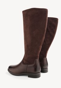 Bottes marron jusqu'aux genoux avec une pointe en cuir lisse et une tige en suède doux. Couture d'accent le long de la semelle et un talon bas et durable.