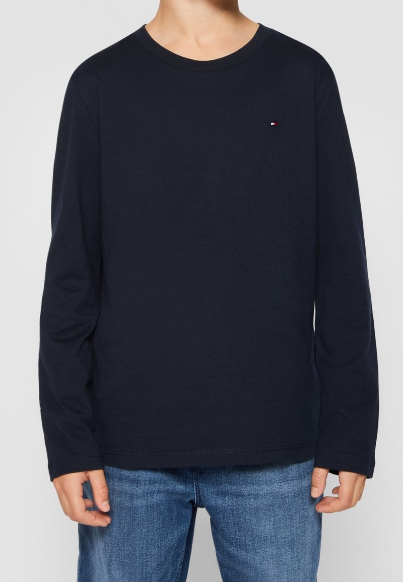 Marinblå långärmad T-shirt i bomull; har en rundad halsringning och en liten logotypdetalj på bröstet. Matchad med blå jeans.