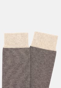 Pletené ponožky s tmavě šedým tělem a světlými béžovými žebrovanými manžetami, které mají strukturovaný vzor a hladký povrch.