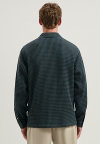 Ciemnozielona koszula o teksturowanym wykończeniu z wzorem wafelka, z długimi rękawami i zapięciem na guziki przy mankietach. Projekt z kołnierzykiem typu notch oraz luźny krój.