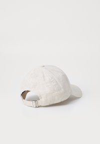 Beige bomullcap med buet skjerm, teksturert stoff, justerbar stropp bak, og uten synlige mønstre eller logoer.