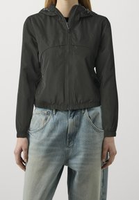 Svart lättvikts zip-up jacka med huva, med elastiska muddar och fåll, buren över högmidjade slitna blå jeans.