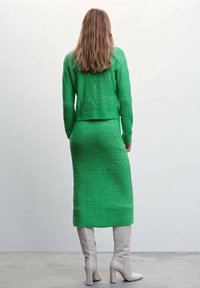 Grüner gestrickter Pullover und passender Rock, strukturierten Stoff, figurbetonter Schnitt, kombiniert mit kniehohen, off-white Stiefeln mit Absatz.
