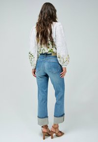 Jeans de mezclilla con un lavado claro, con puños enrollados, combinados con una blusa blanca de estampado floral con mangas abullonadas y detalles de costura visibles.