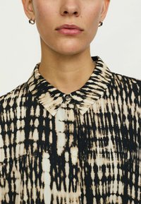 Cămașă cu guler, având un model abstract în nuanțe de negru și bej, confecționată dintr-un material ușor; include o detaliu cu nasture la gât.