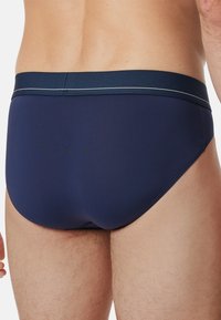 Marineblauwe zwembroek met een gladde textuur en een contrasterende tailleband met een dunne witte streep. Ontworpen voor minimale bedekking.