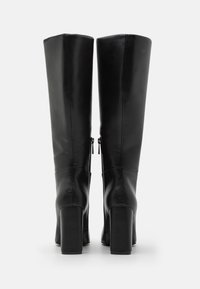 Schwarze kniehohe Stiefel aus glattem Leder, mit einem Reißverschluss auf der Rückseite, eckiger Zehenpartie und klobigen hohen Absätzen.