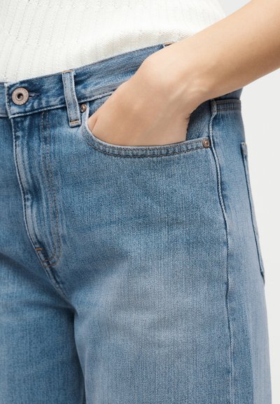 Χέρι τοποθετημένο στην μπροστινή τσέπη ανοιχτόχρωμων τζιν με λευκό πλεκτό τοπ.