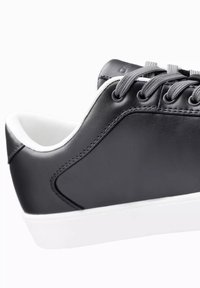 Czarny skórzany sneakers z szarymi sznurowadłami, białą podeszwą, gładką teksturą, zaokrąglonym kształtem i kontrastującymi detalami ściegów po bokach.