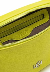 Interior de bolsa de cuero verde lima con un acabado texturizado, presenta un bolsillo con cremallera y un forro marrón, con marca grabada visible.