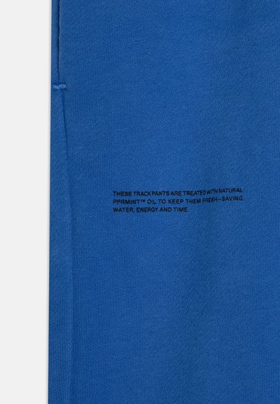 Pantalones deportivos azules hechos de una tela suave, con corte recto. Texto impreso en negro detallando el tratamiento con aceite natural para mayor frescura.