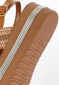 Brown platform sandal featuring a woven straw upper and a thick textured sole with silver and gold metallic accents along the side.