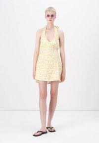 Geel bloemen mini-jurk met een halterhalslijn, versierd met witte bloemen, een aansluitend lijfje en een uitlopende rok. Droeg het met zwarte slippers.