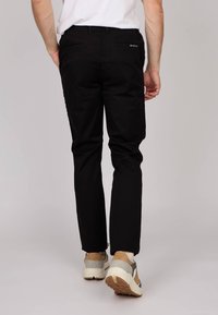 Pantalons en coton noirs avec une coupe slim et deux poches arrière. Portés avec des baskets claires présentant un mélange de gris et de beige.