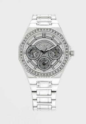 Montre bracelet Guess en métal argenté avec une lunette ornée de cristaux, trois sous-cadrans affichant l'heure sur 24 heures, le jour et la date sur un cadran texturé détaillé.