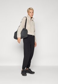 Pull-over en polaire beige à demi-fermeture, associé à un pantalon de survêtement noir et des chaussures de sport. Portant un sac à épaule noir. Design simple, texture douce.